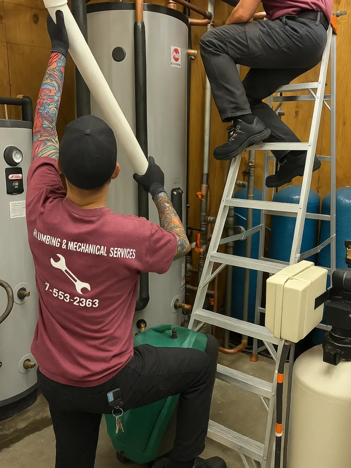 Two workers on ladders installing pipes in a mechanical room, with tanks and equipment nearby.