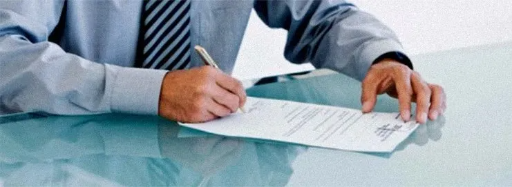 Person in a dress shirt signing documents at a desk with another hand resting nearby