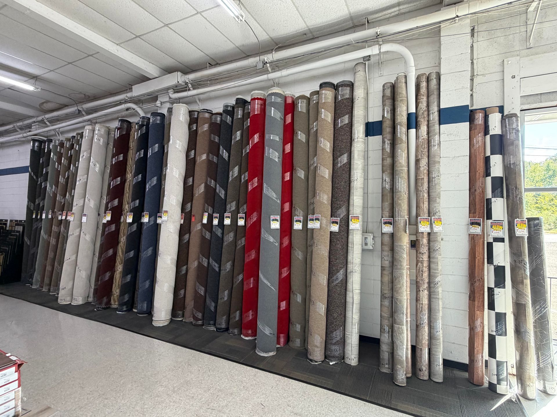 Rows of rolled carpets and rugs displayed vertically in a store aisle, with assorted colors and patterns.