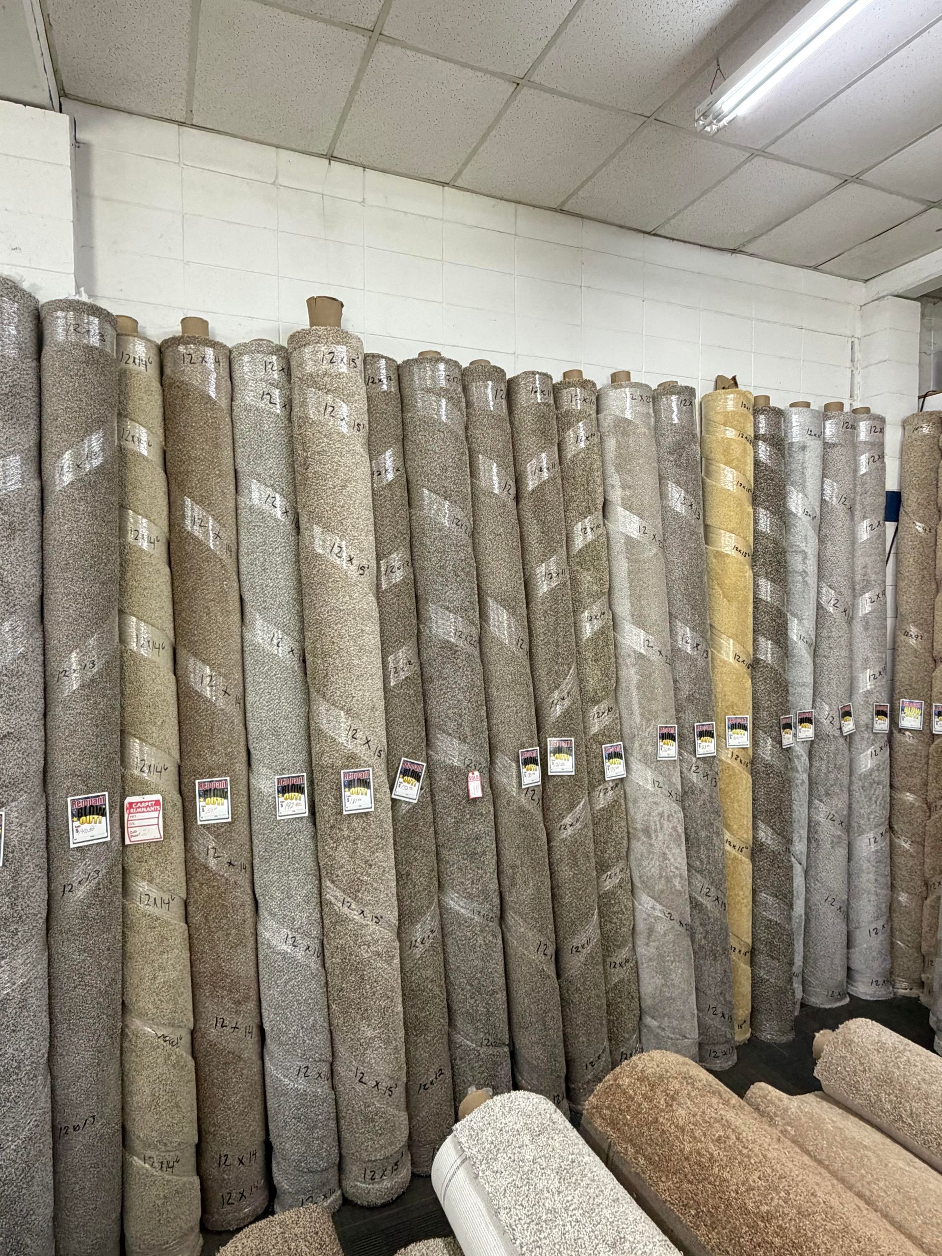 Rows of rolled carpet samples in a flooring showroom, mostly gray and beige patterns.