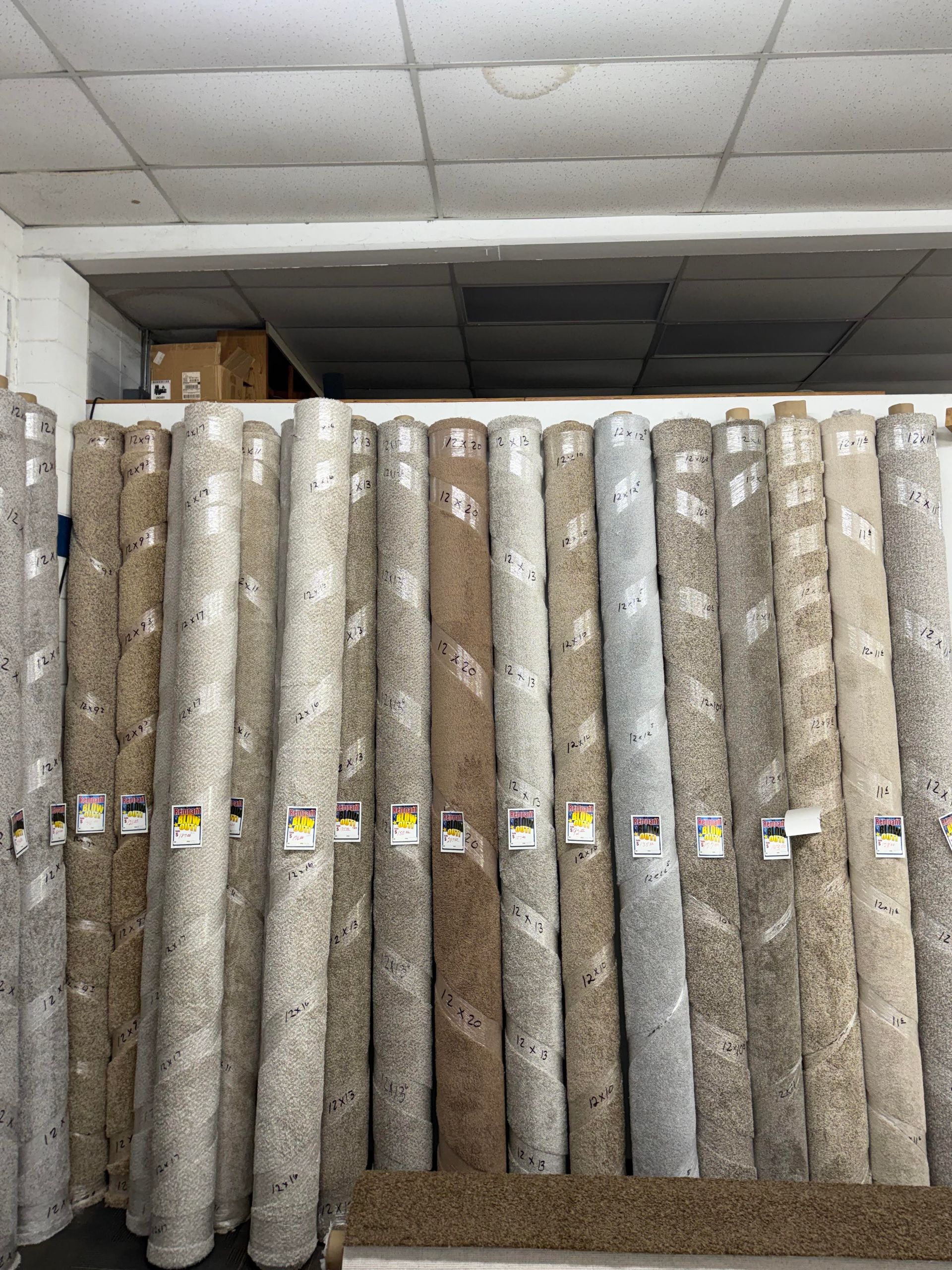 Rolled carpets stacked upright in a warehouse aisle under fluorescent lighting