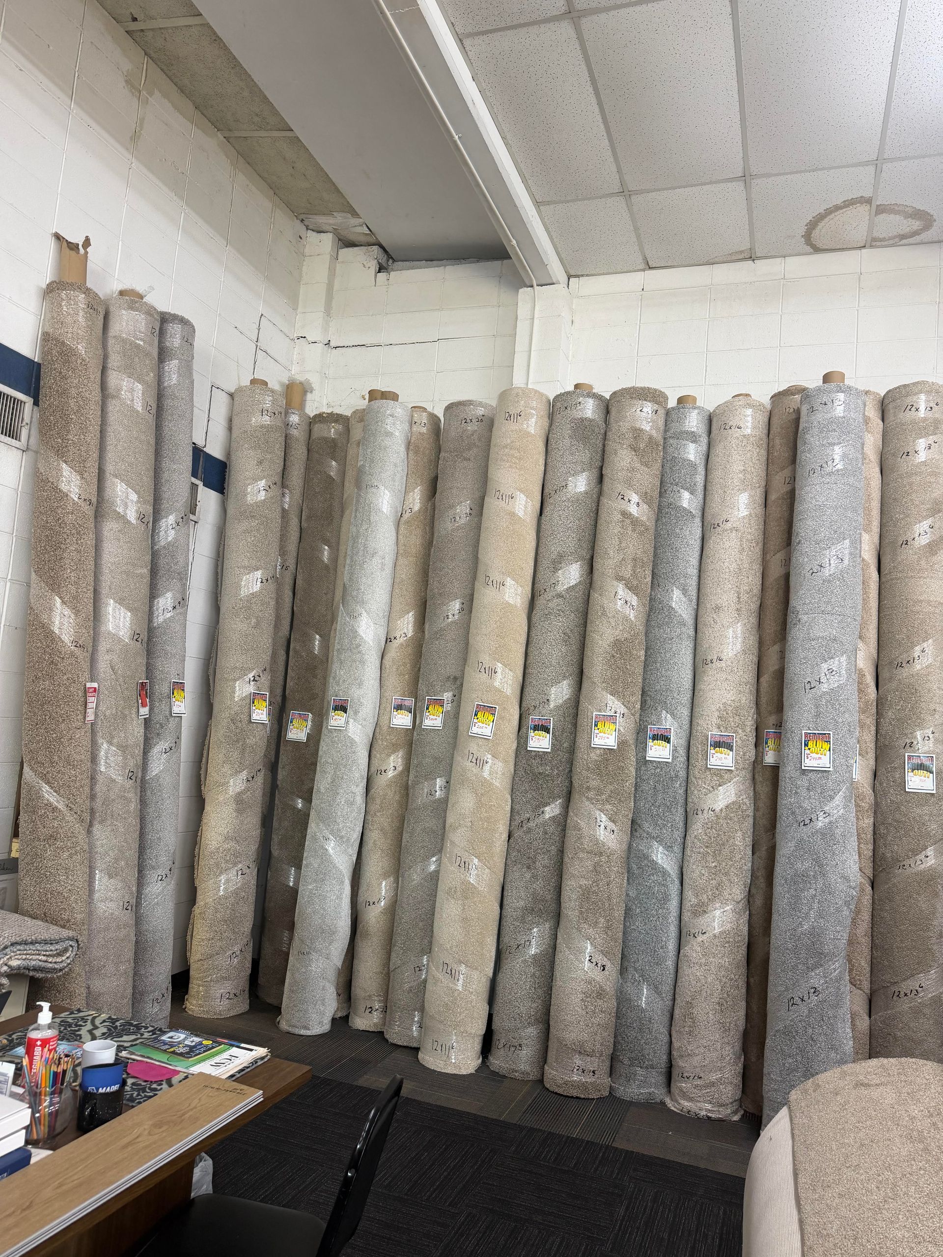 Rolled carpets stacked upright in a storage room beside a table with supplies.