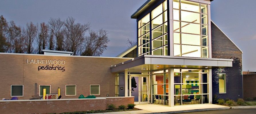 Modern brick pediatric clinic at dusk with lit glass entrance and sign.