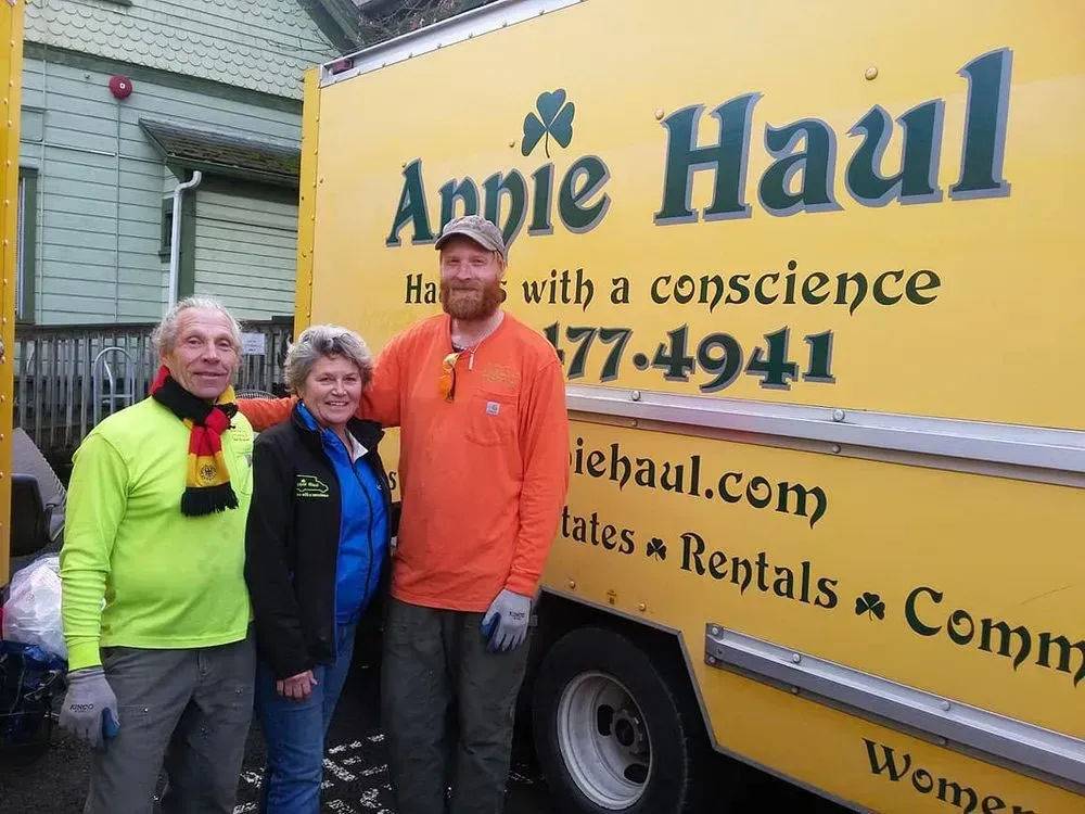 Three people stand in front of a yellow moving truck; the logo reads 