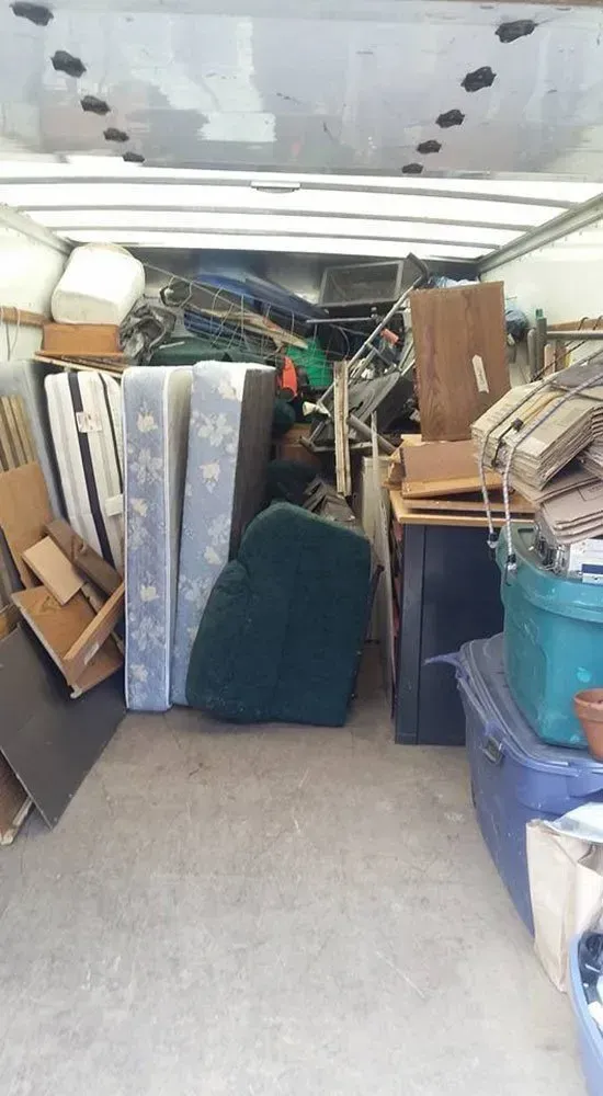 Interior of a moving truck filled with furniture, mattresses, and miscellaneous items.