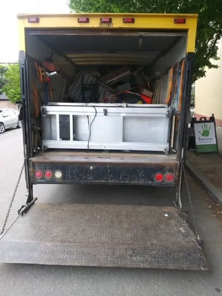 Open back of a yellow truck loaded with various items, including a large silver unit.