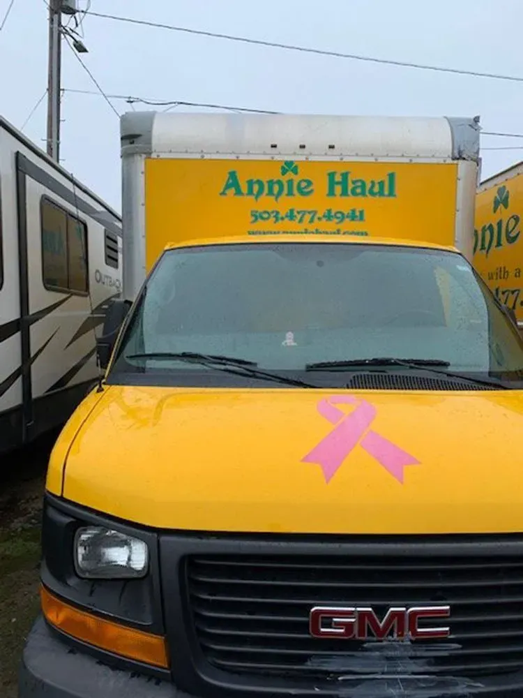 Yellow Annie Haul truck with pink ribbon, parked.