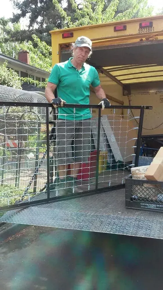 Man in green shirt holds metal gate on a truck ramp, sunny day.