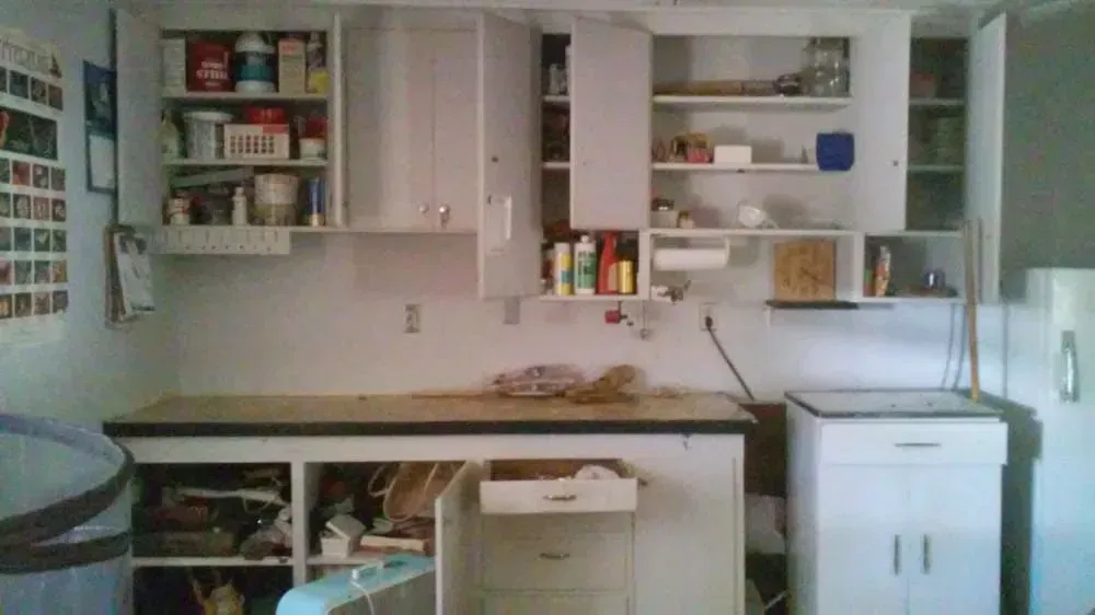 A cluttered white kitchen with open cabinets above a wooden countertop.