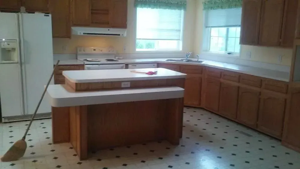 Kitchen with wooden cabinets, white appliances, island, and window. Black and white patterned floor.