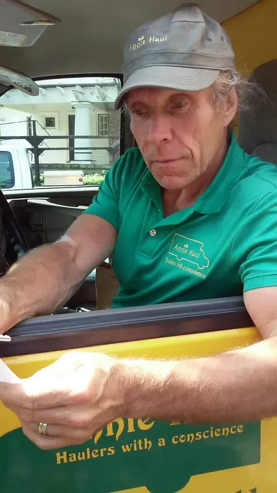 Man in green shirt and cap, inside vehicle. Holding a document; logo reads, 