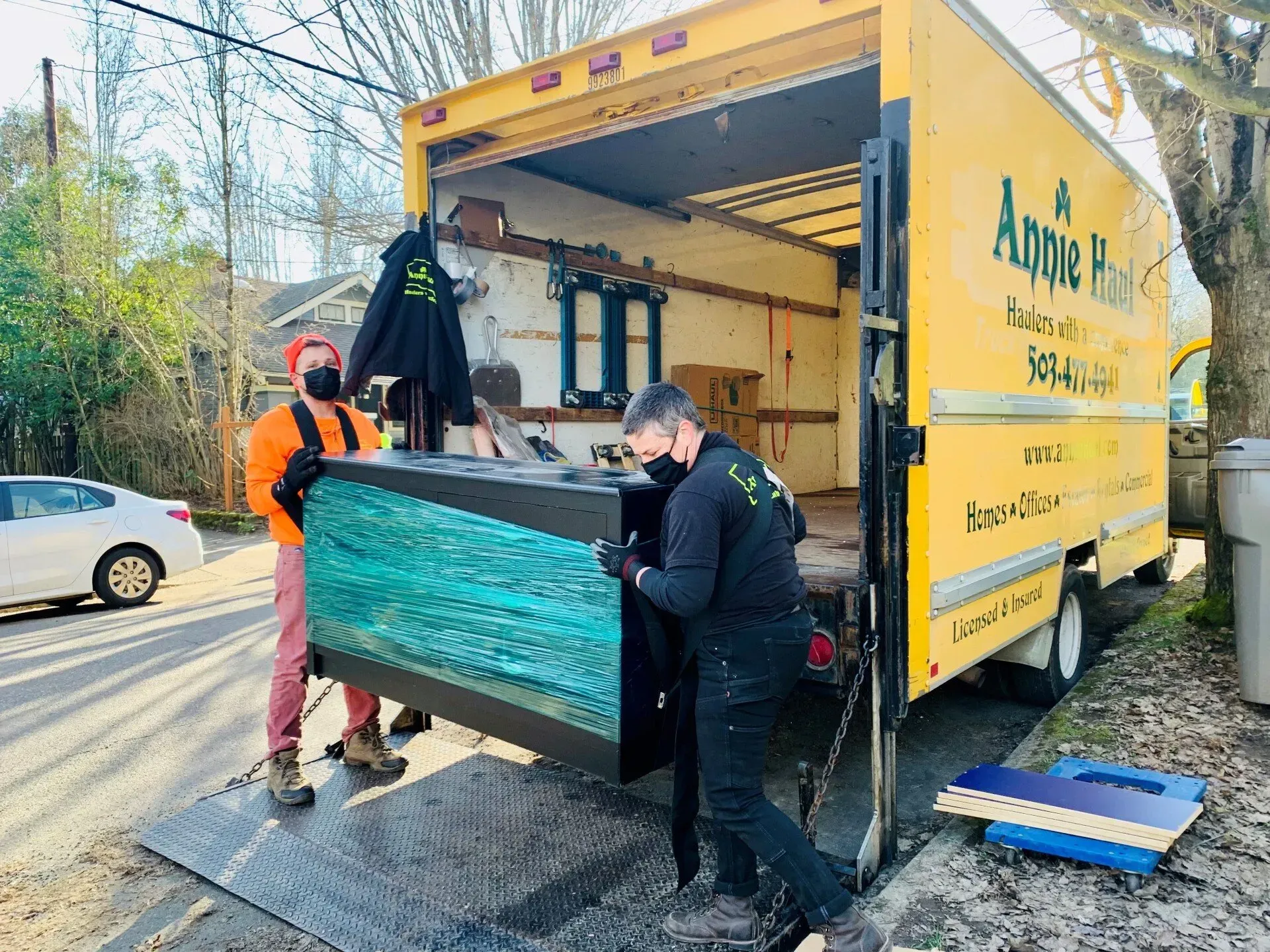 Two people wearing masks load a large aquarium into a moving truck.