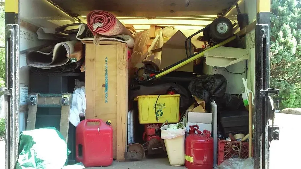 Inside of a moving truck filled with various items, including boxes, a rug, and containers.
