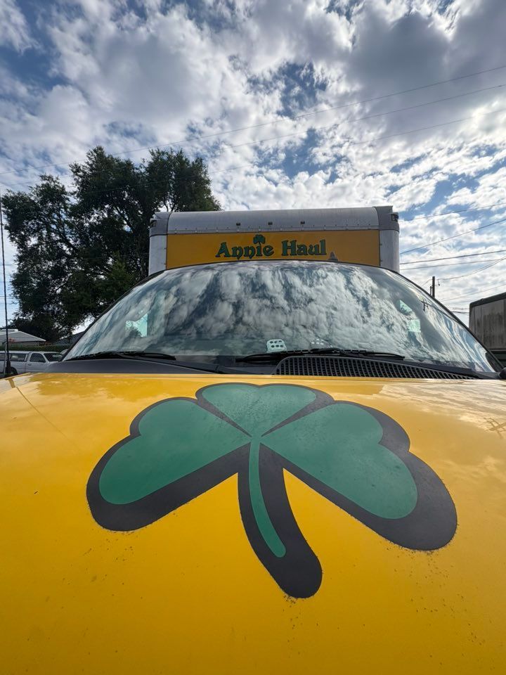 Yellow vehicle hood with a green shamrock decal; a trailer is in the background.