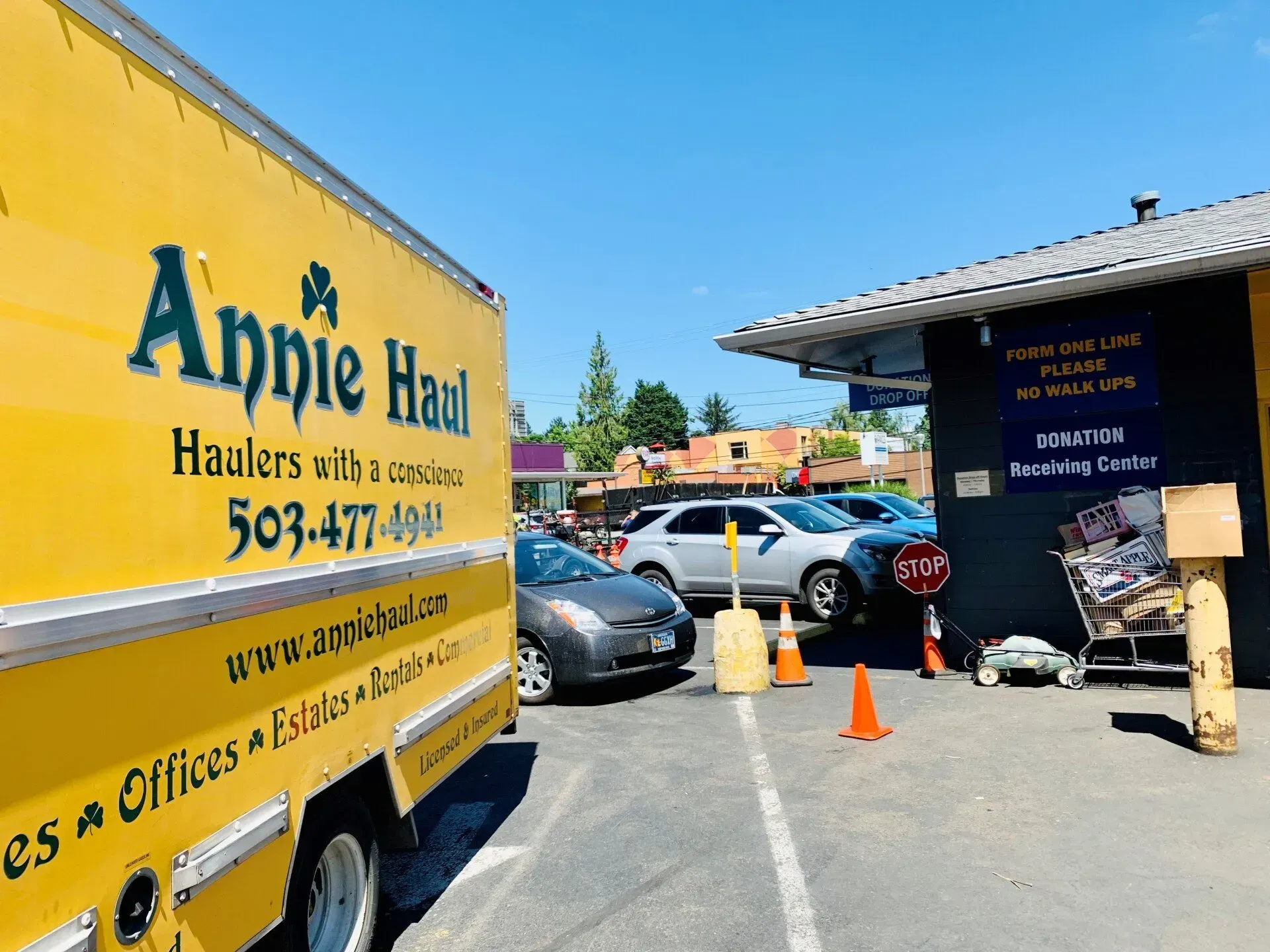 Yellow Annie Haul moving truck parked by a building with cars, cones, and signs in a parking lot.