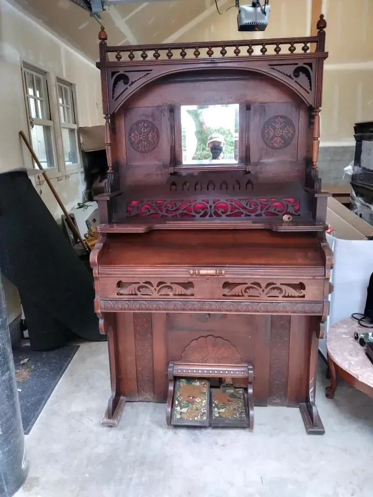 Antique organ with ornate wooden carvings, in a garage setting.