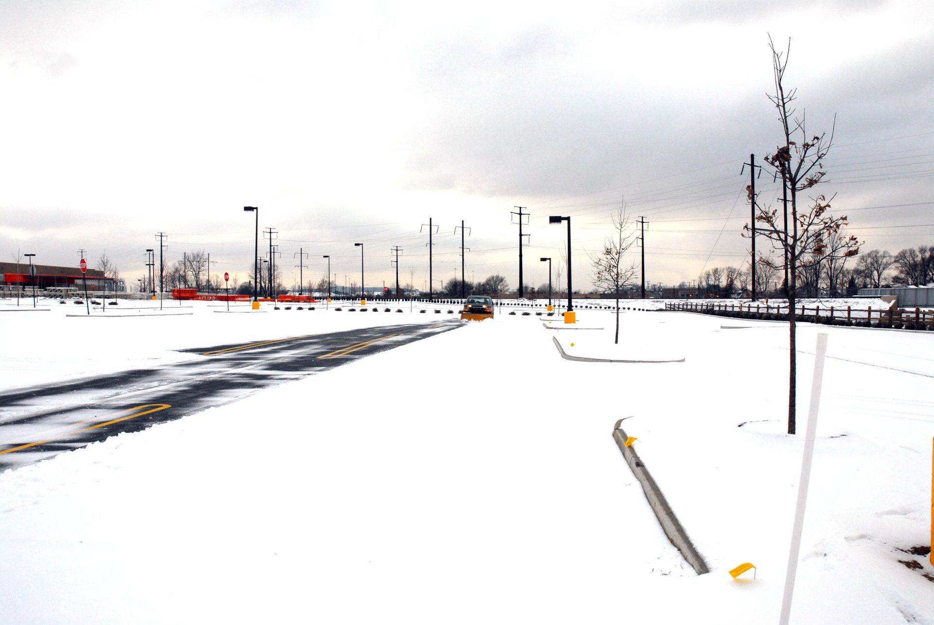 Snow-covered parking lot with streetlights under a cloudy sky.