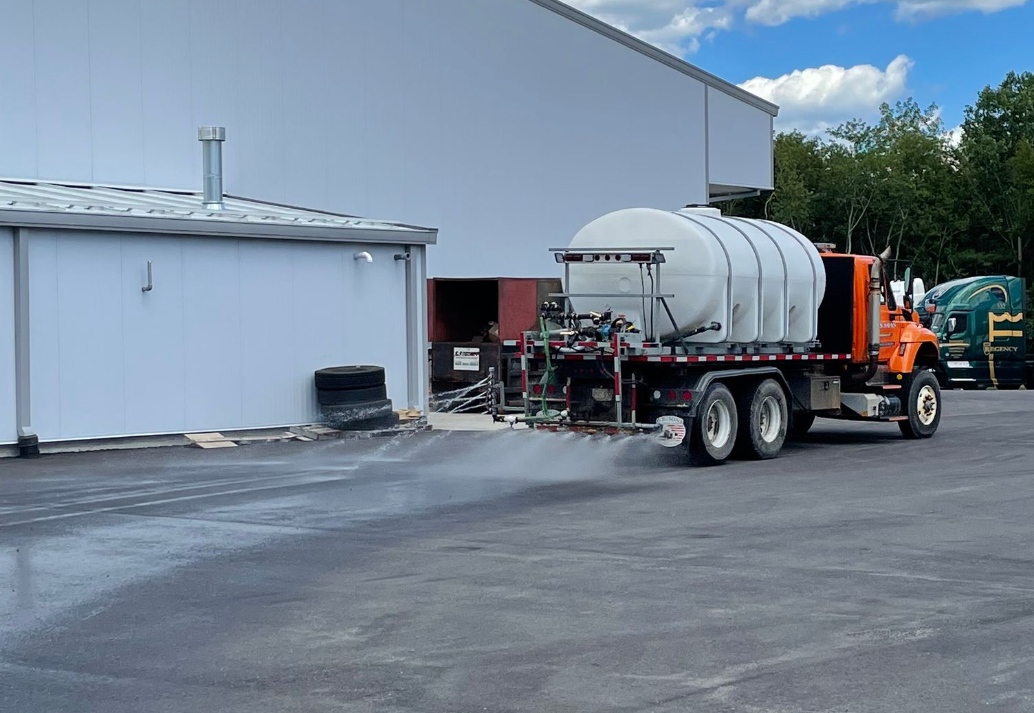 Orange truck spraying a liquid on asphalt in front of a building.