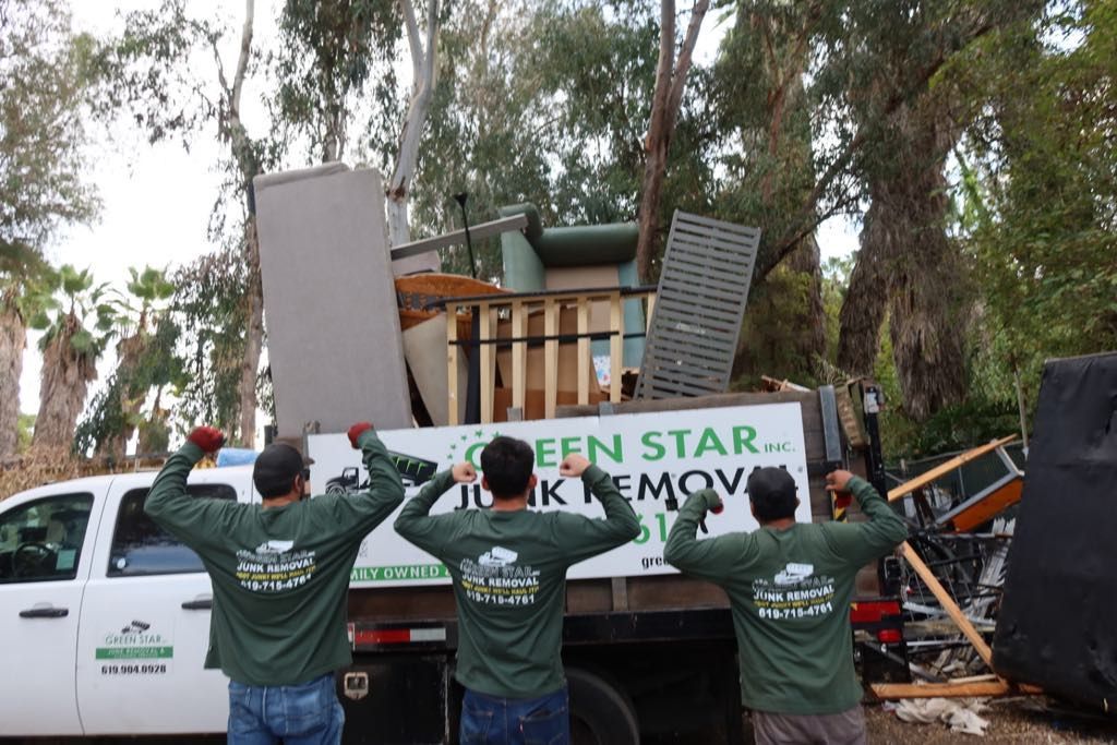 Three men flex with a full truck of junk. Green Star Junk Removal truck in front of trees.