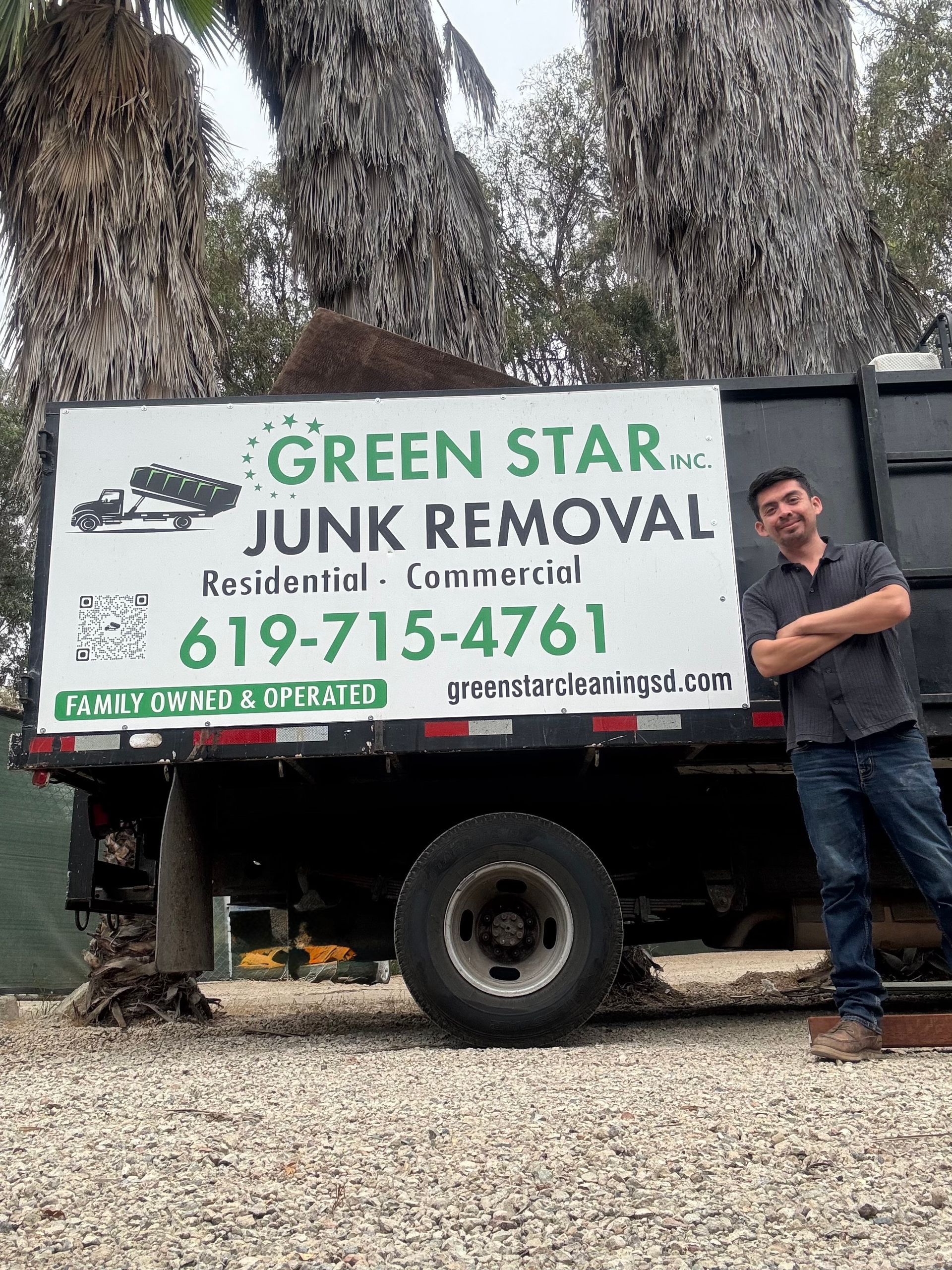 Man standing beside a Green Star Junk Removal truck. The truck has a green and white logo, and is parked outdoors.