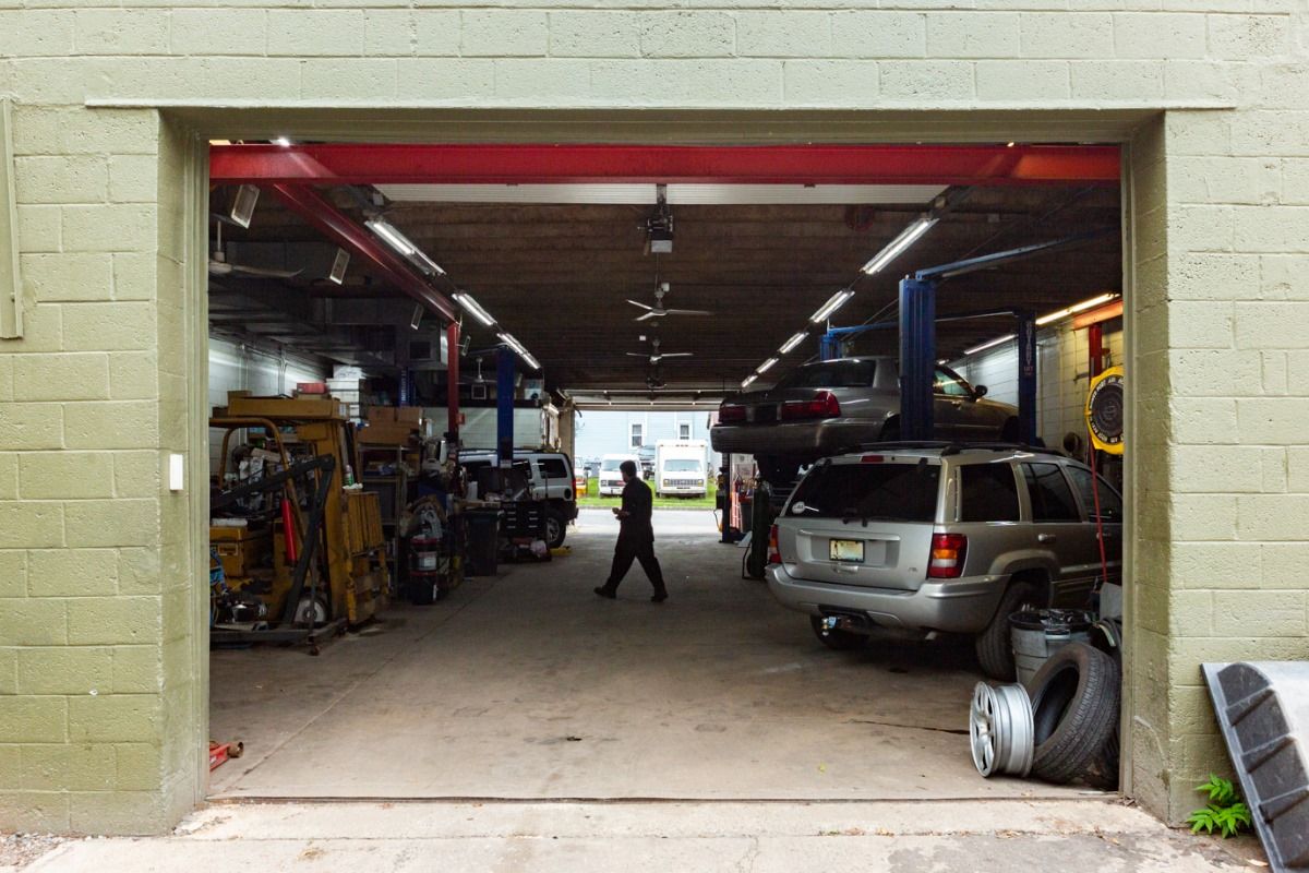 Open garage entrance; interior shows auto repair shop with cars on lifts, worker walking.