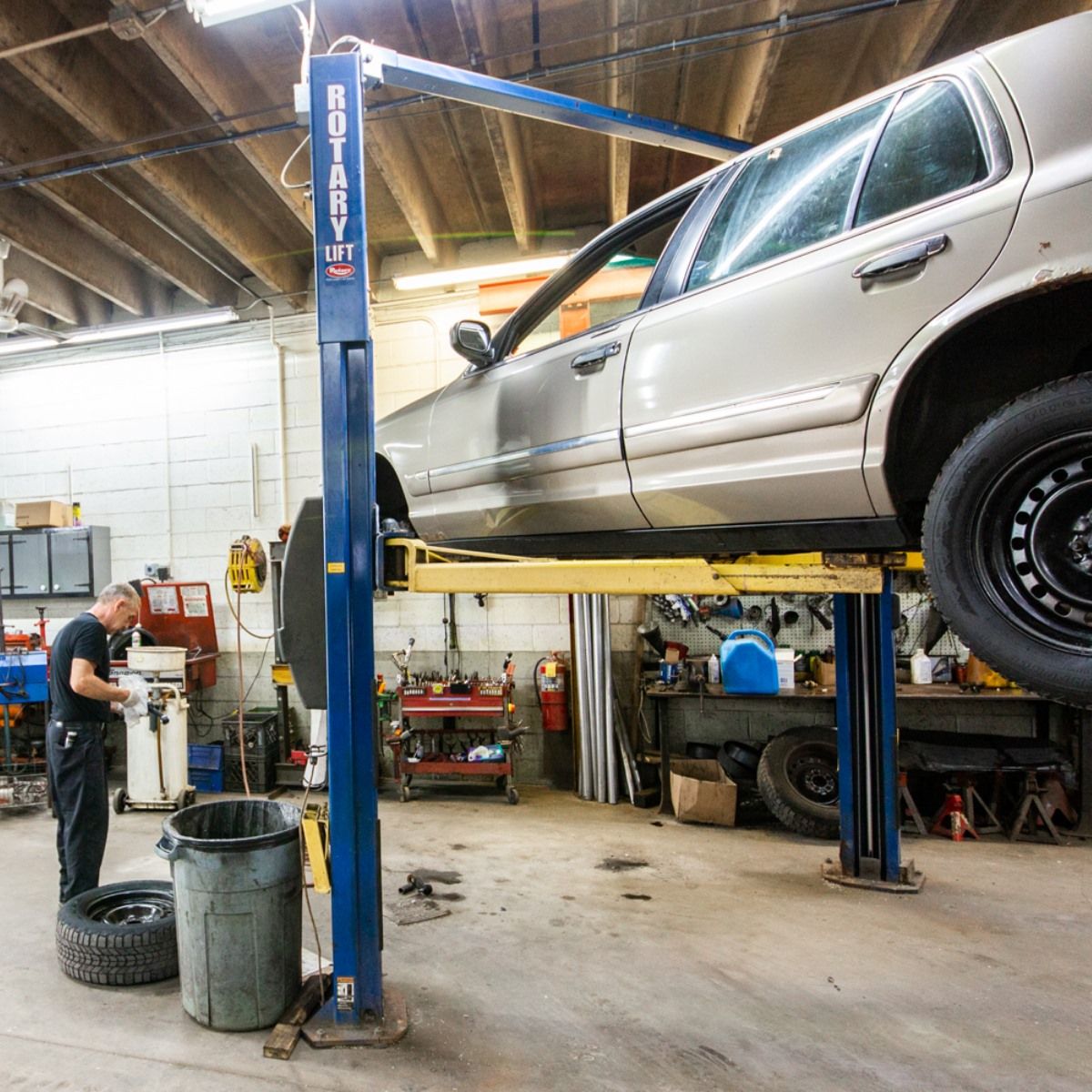 Mechanic working under a silver car raised on a lift in a garage.
