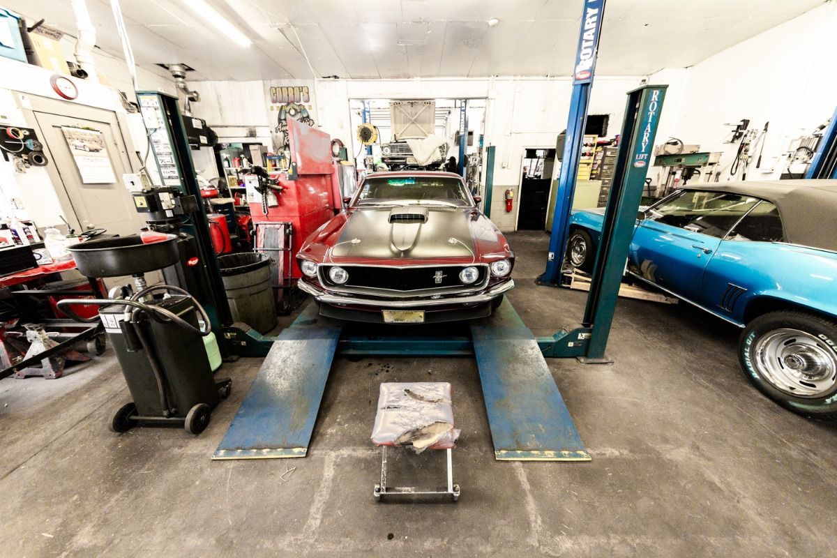 Classic maroon car raised on a lift in a garage, next to a blue car.