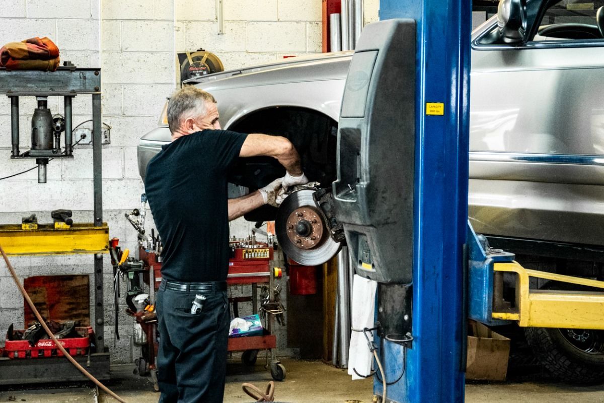 Mechanic working on car's brakes in a garage. Car is elevated on a blue lift.