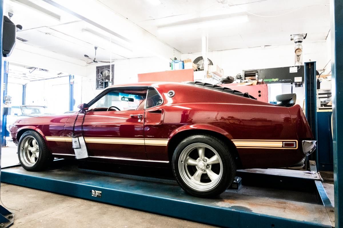 Red classic muscle car raised on a lift inside a mechanic's shop.