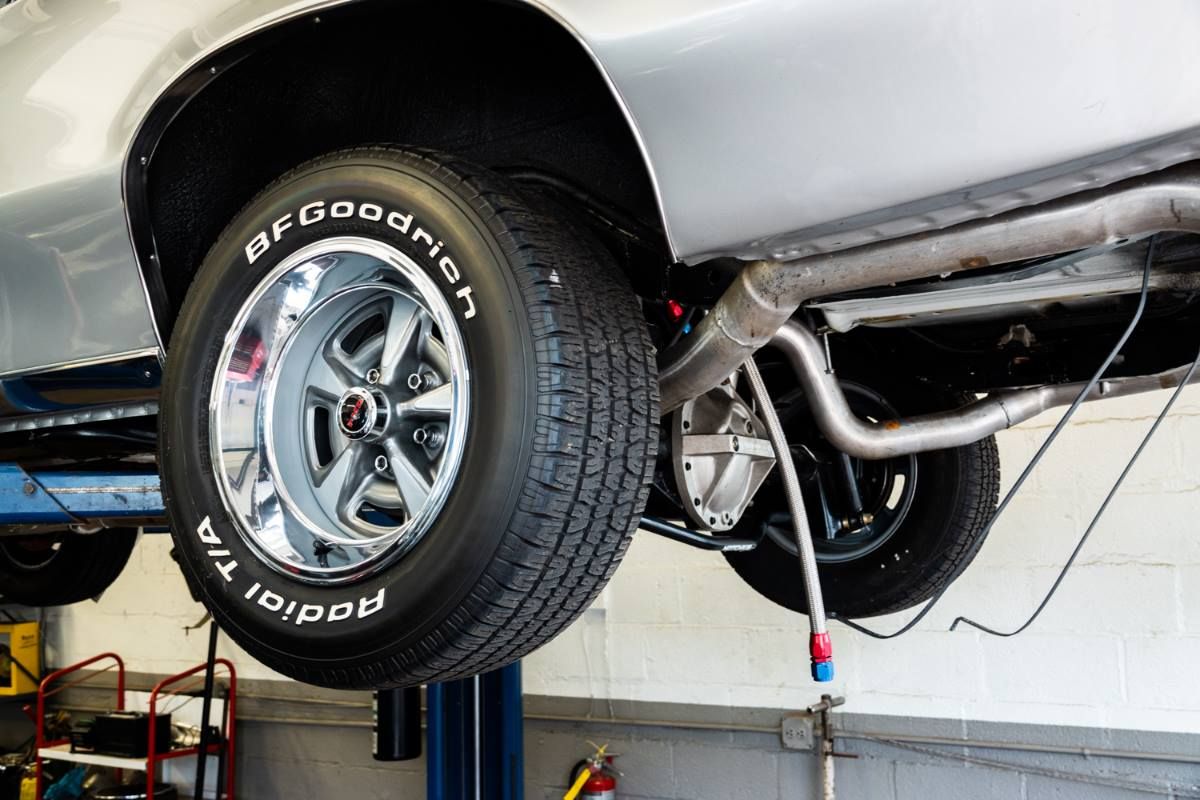 Silver classic car raised on a lift, tires and undercarriage visible.