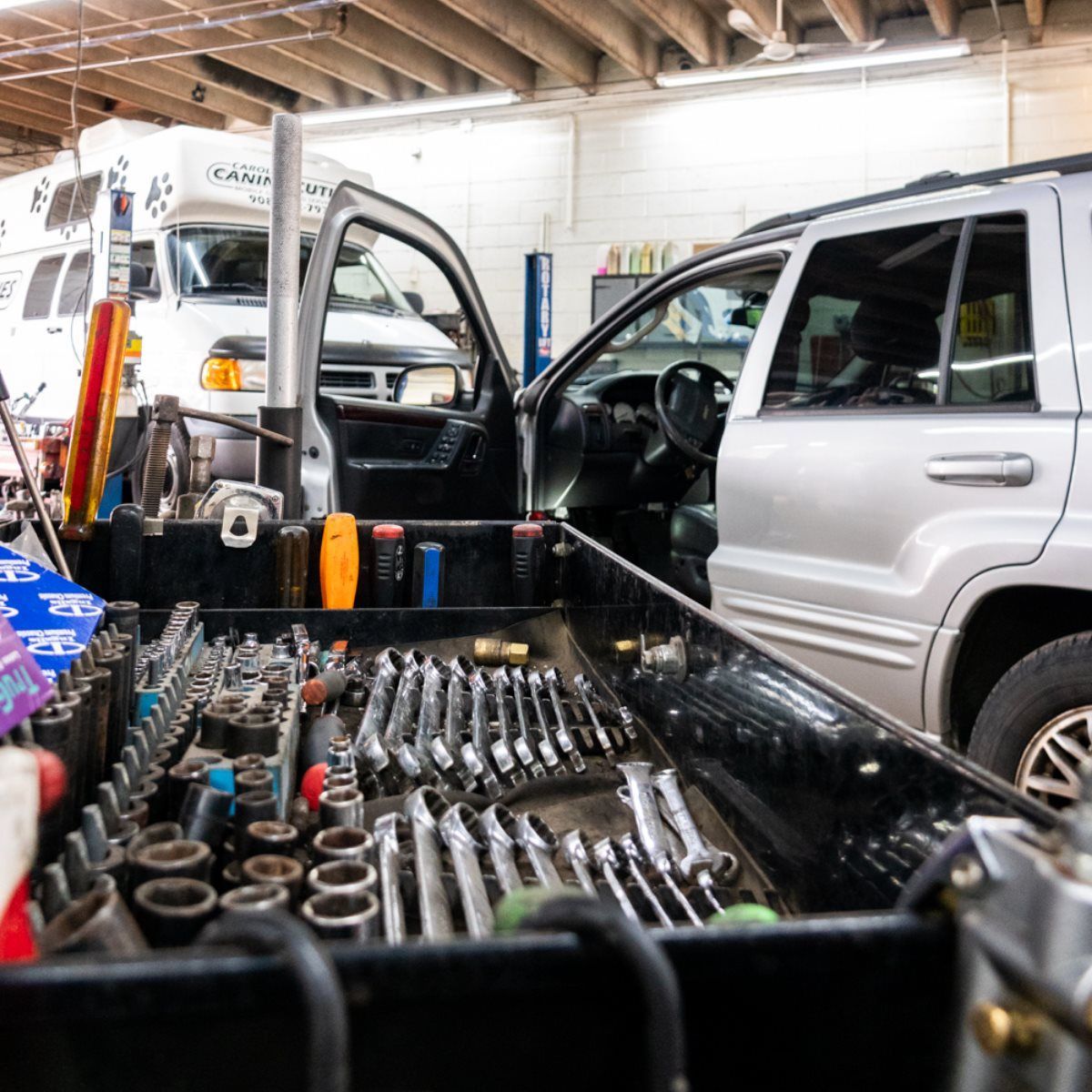 Toolbox filled with tools in a garage, next to a silver SUV with open driver's side door and a white truck.