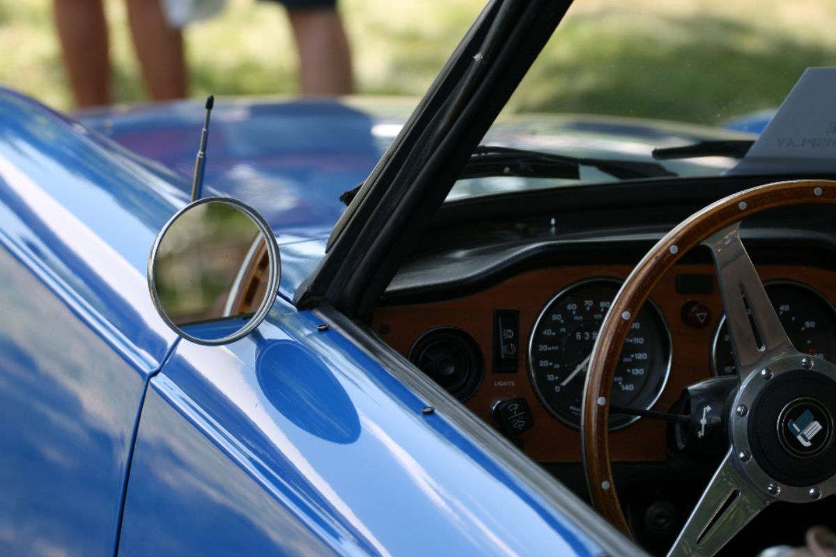 Blue classic car interior with wooden steering wheel and side mirror.