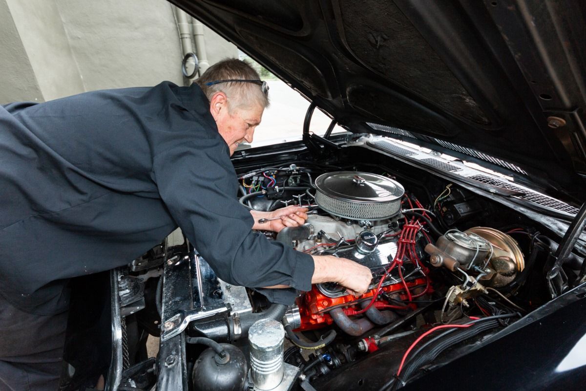 Man working on a classic car engine with a black hood up.