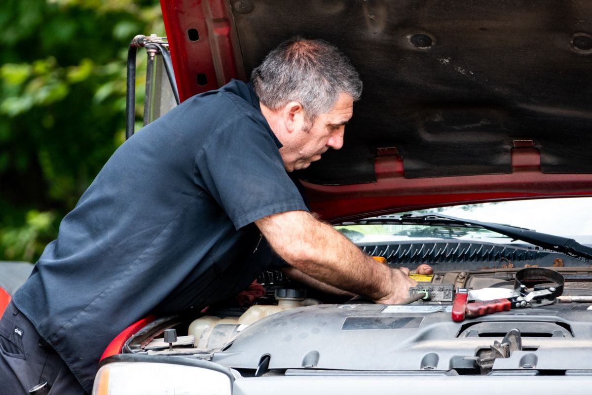 Mechanic working under the hood of a red truck, using tools.