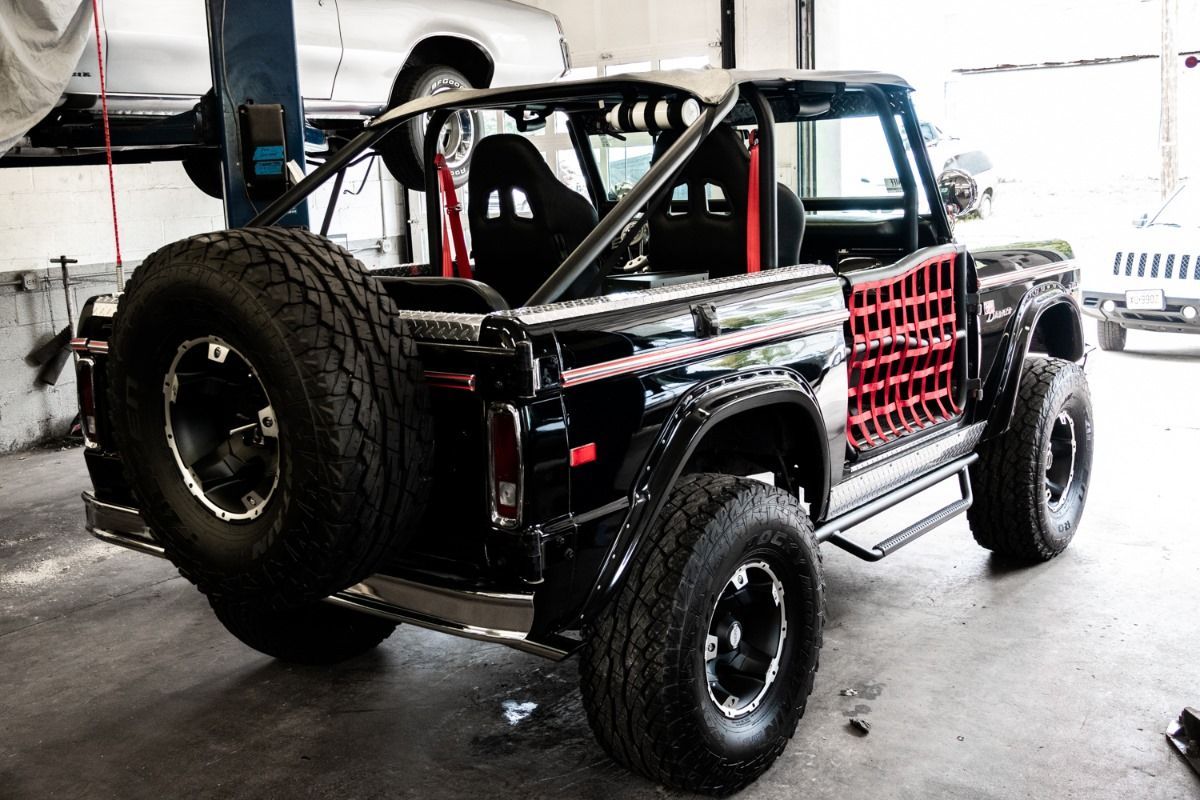Black, modified vintage SUV with roll cage and off-road tires in a garage.