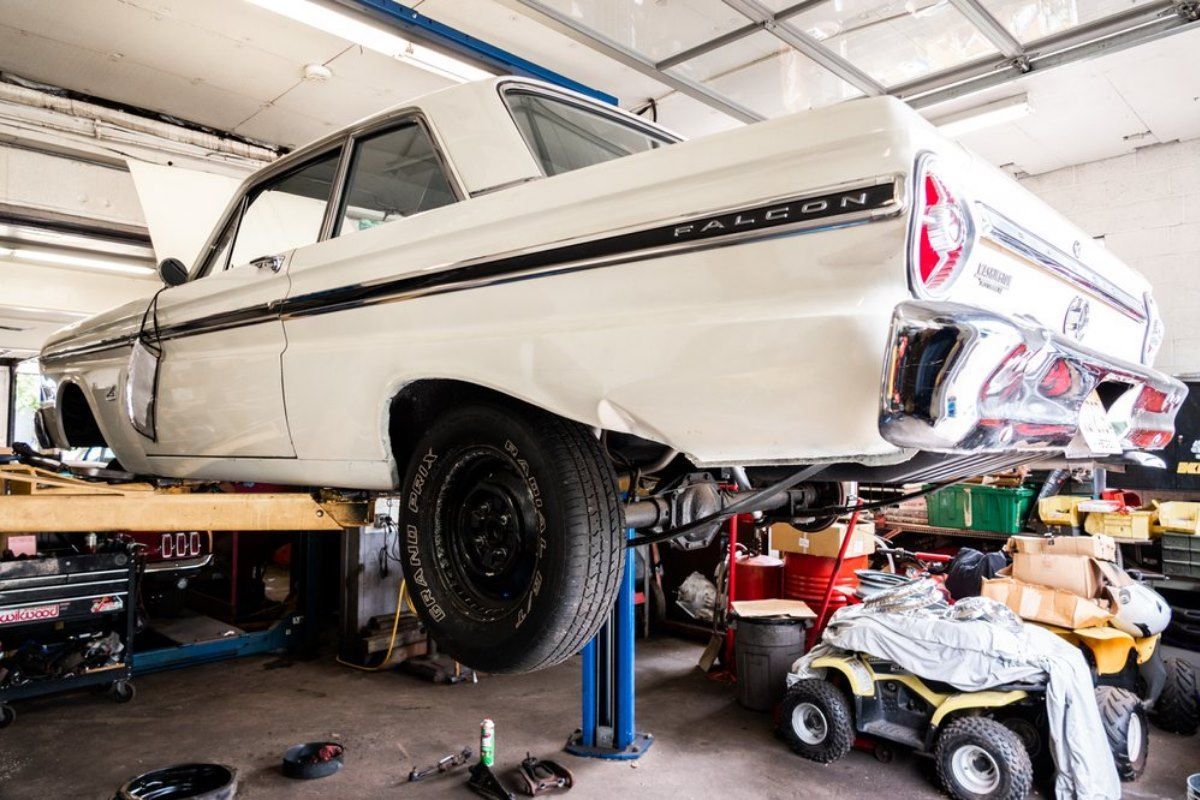 White classic car raised on a lift in a garage, undergoing repair work.