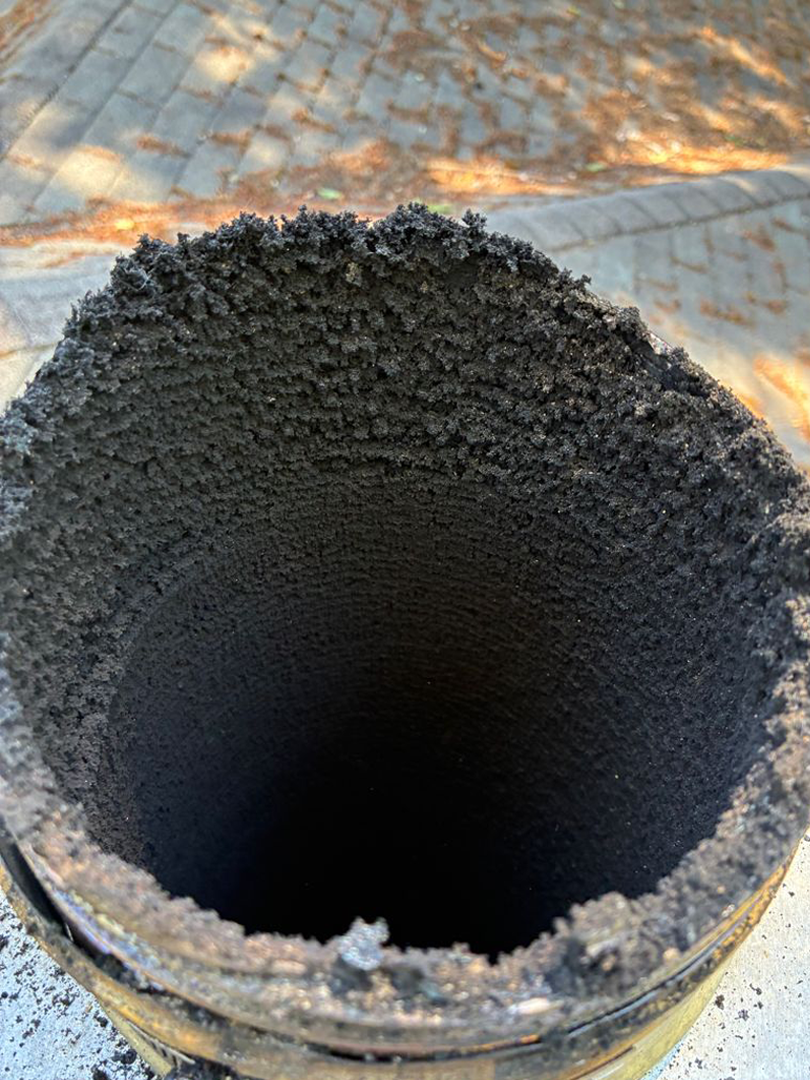 Close-up of a round metal pipe opening with dark soot buildup inside.