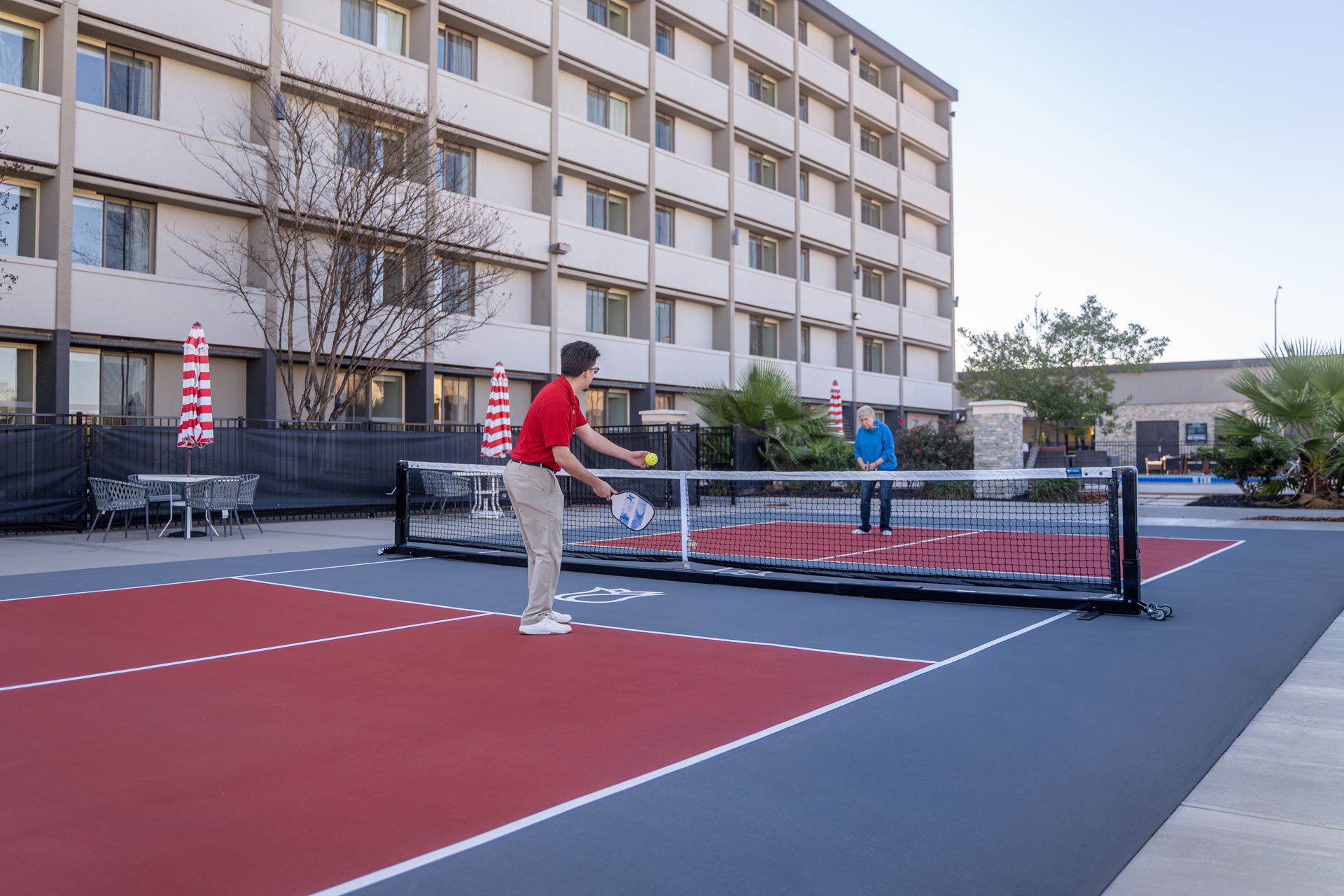 Two people playing pickleball on a court with a multi-story building in the background.