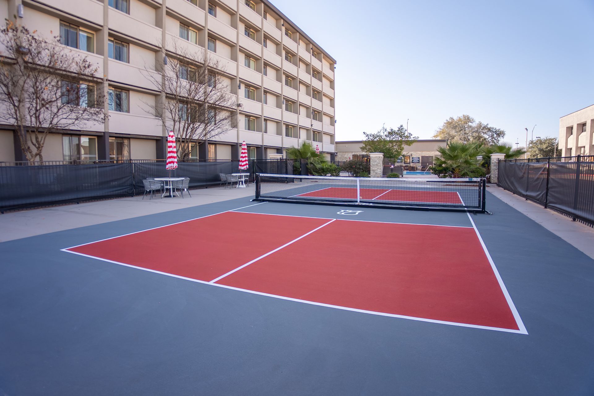 Pickleball court with net, red playing area, and a building in the background.