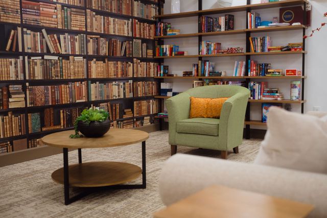 A cozy reading nook with bookshelves, green armchair, round coffee table, and sofa.