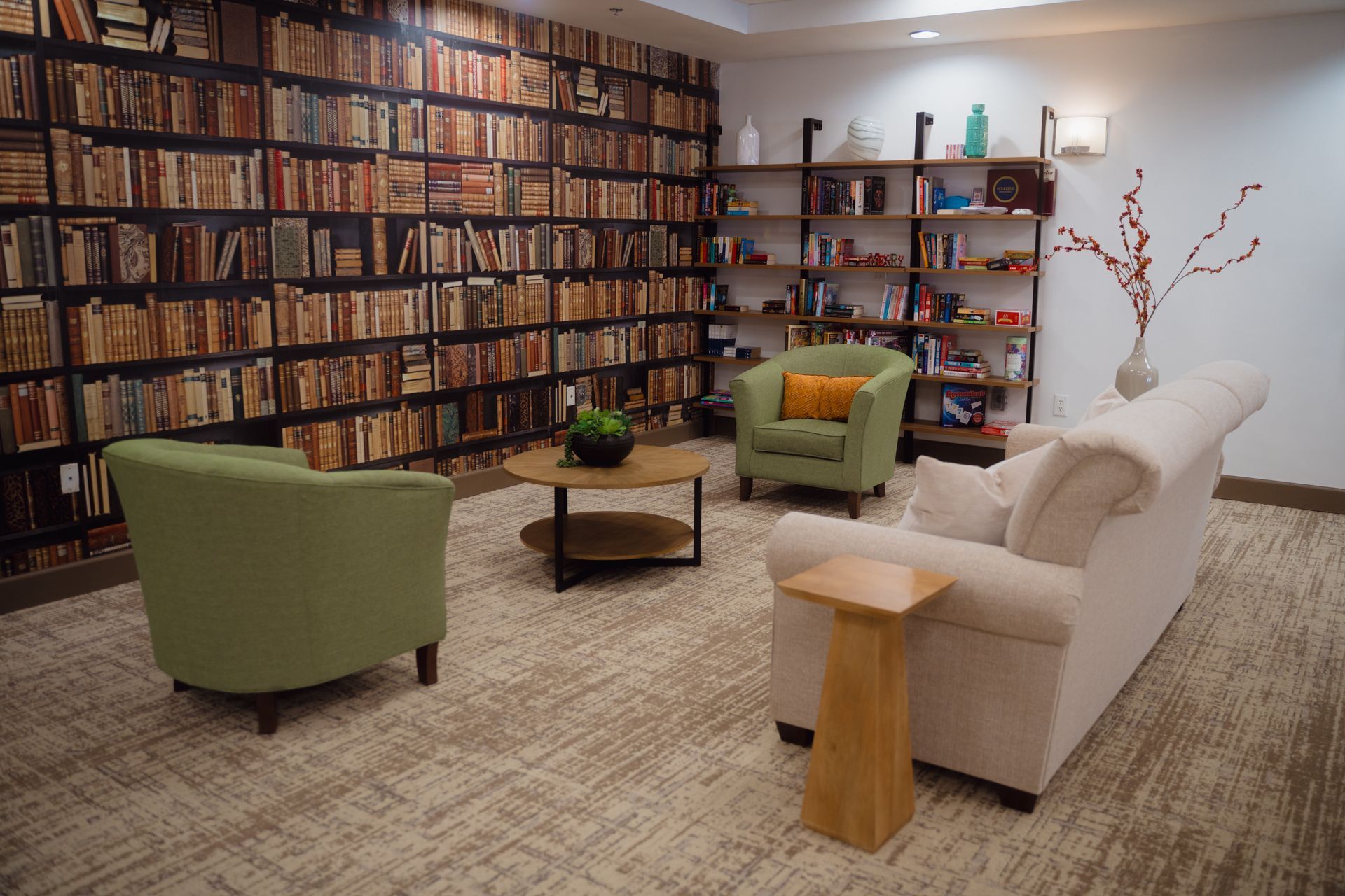 Cozy reading nook with bookshelf wallpaper, armchairs, and a sofa.