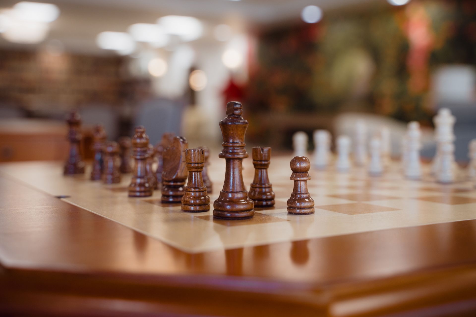 Chess pieces set up on a wooden board, ready for a game. Brown and white pieces in a room.