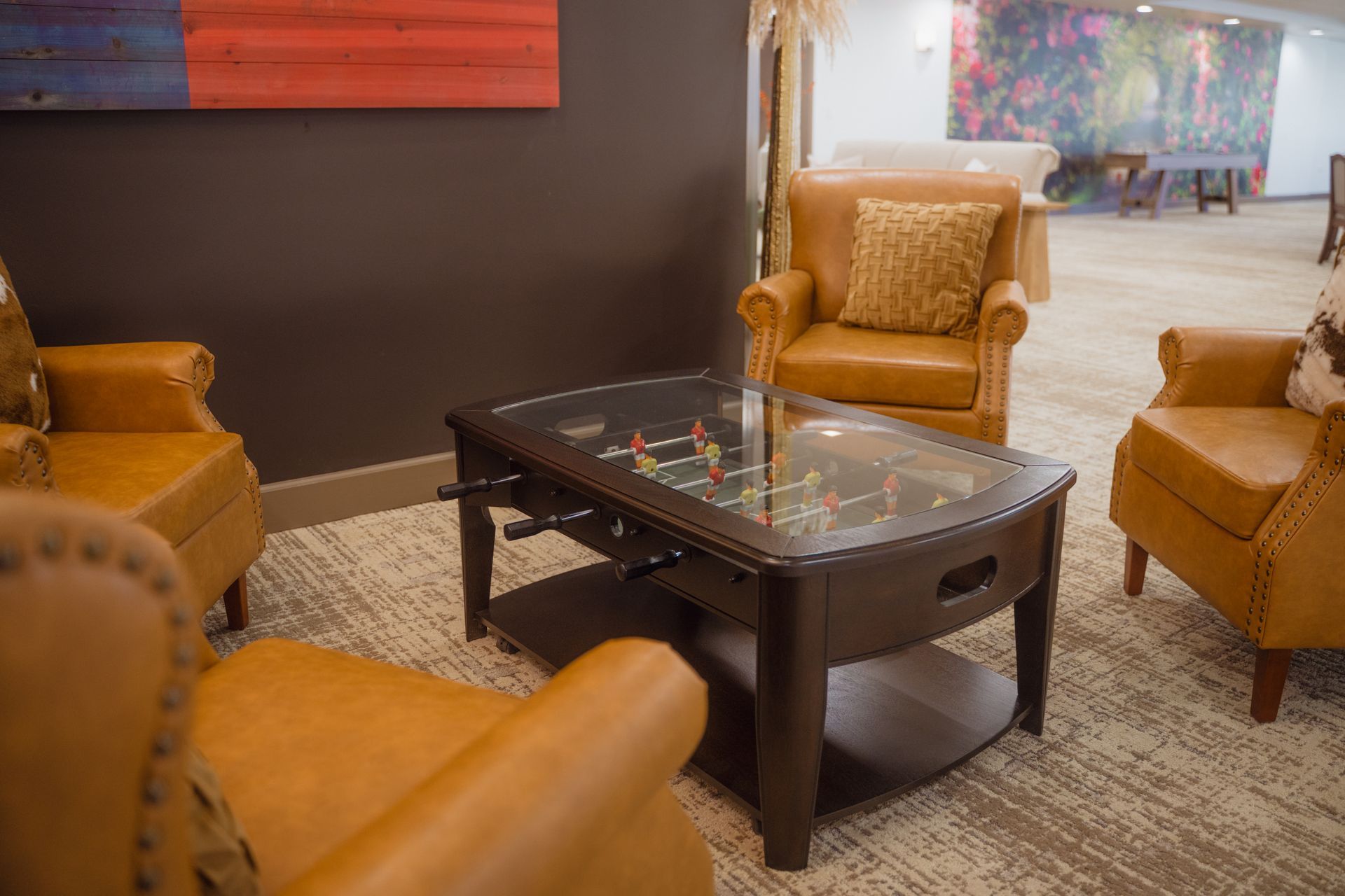 Cozy seating area with a foosball table, brown armchairs, and colorful wall art.