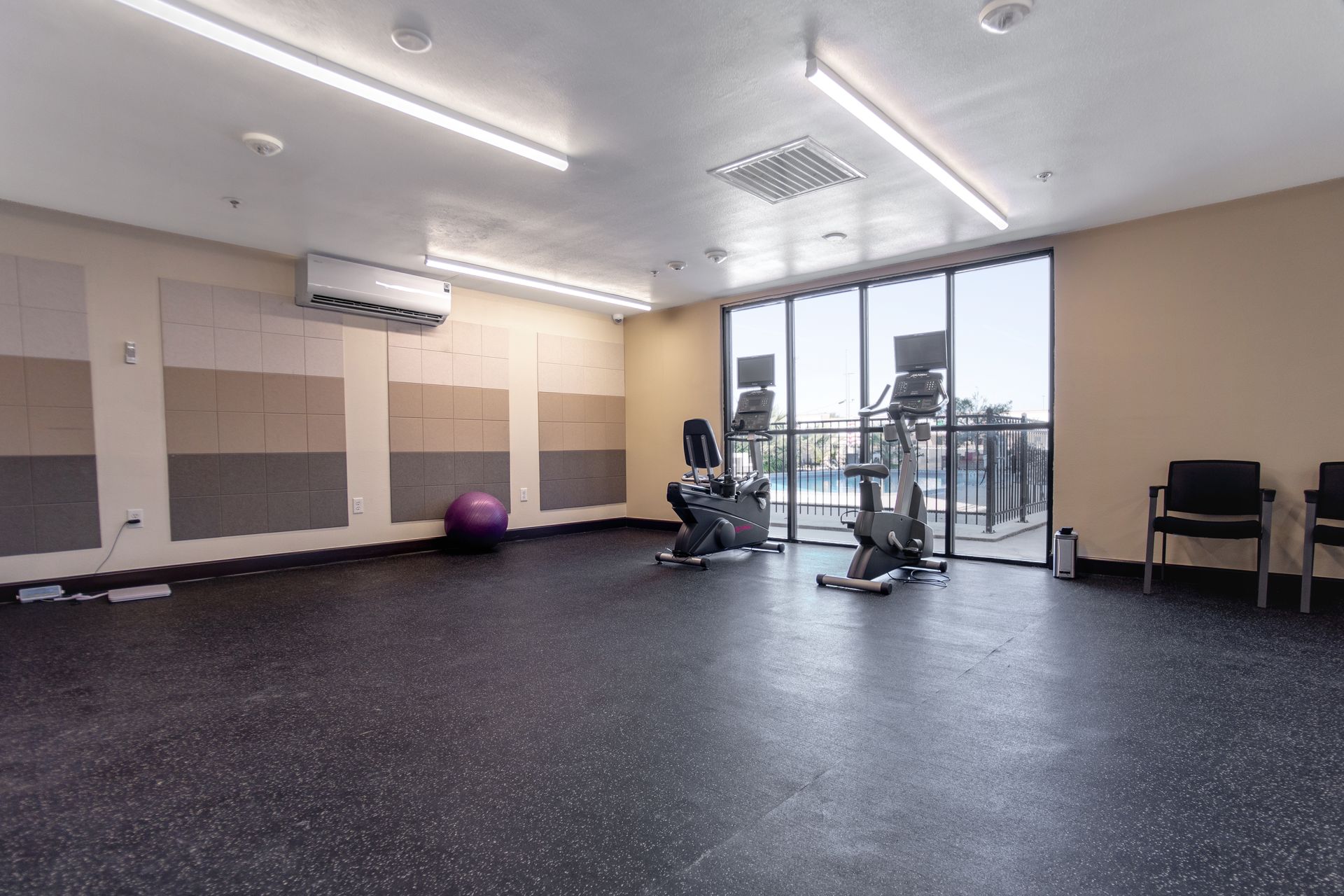 Gym with exercise equipment, including a stationary bike and elliptical machine, with a large window and outdoor view.