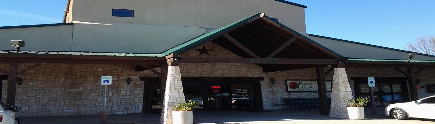 A stone-walled building with a green roof and a covered entrance on a sunny day.
