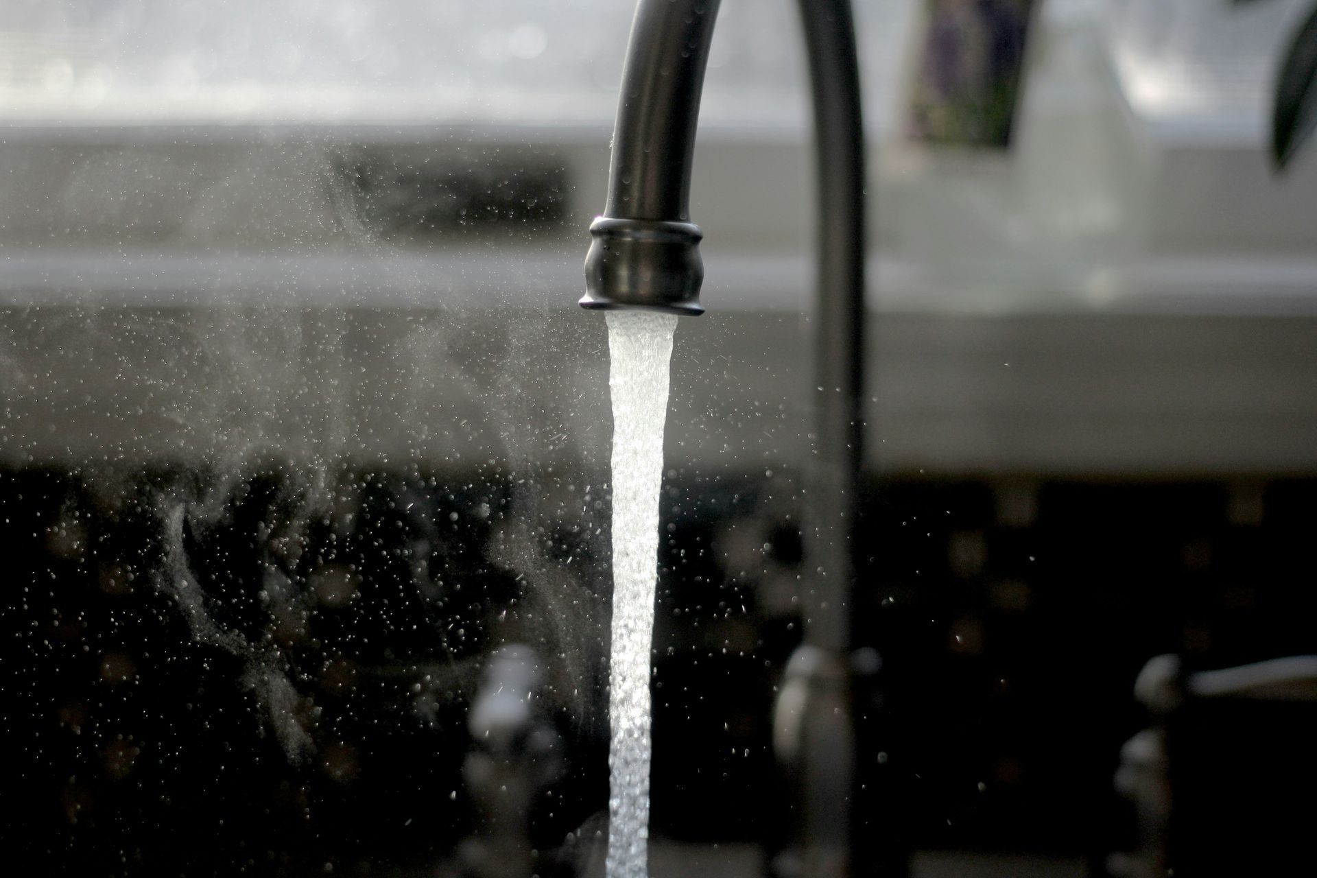 Water streams from a dark metal faucet in a kitchen.