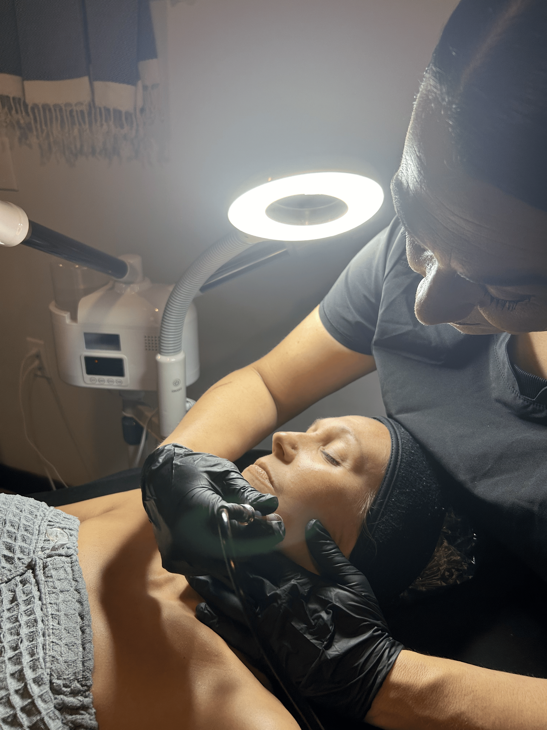 A woman is getting a facial treatment from a man wearing black gloves.