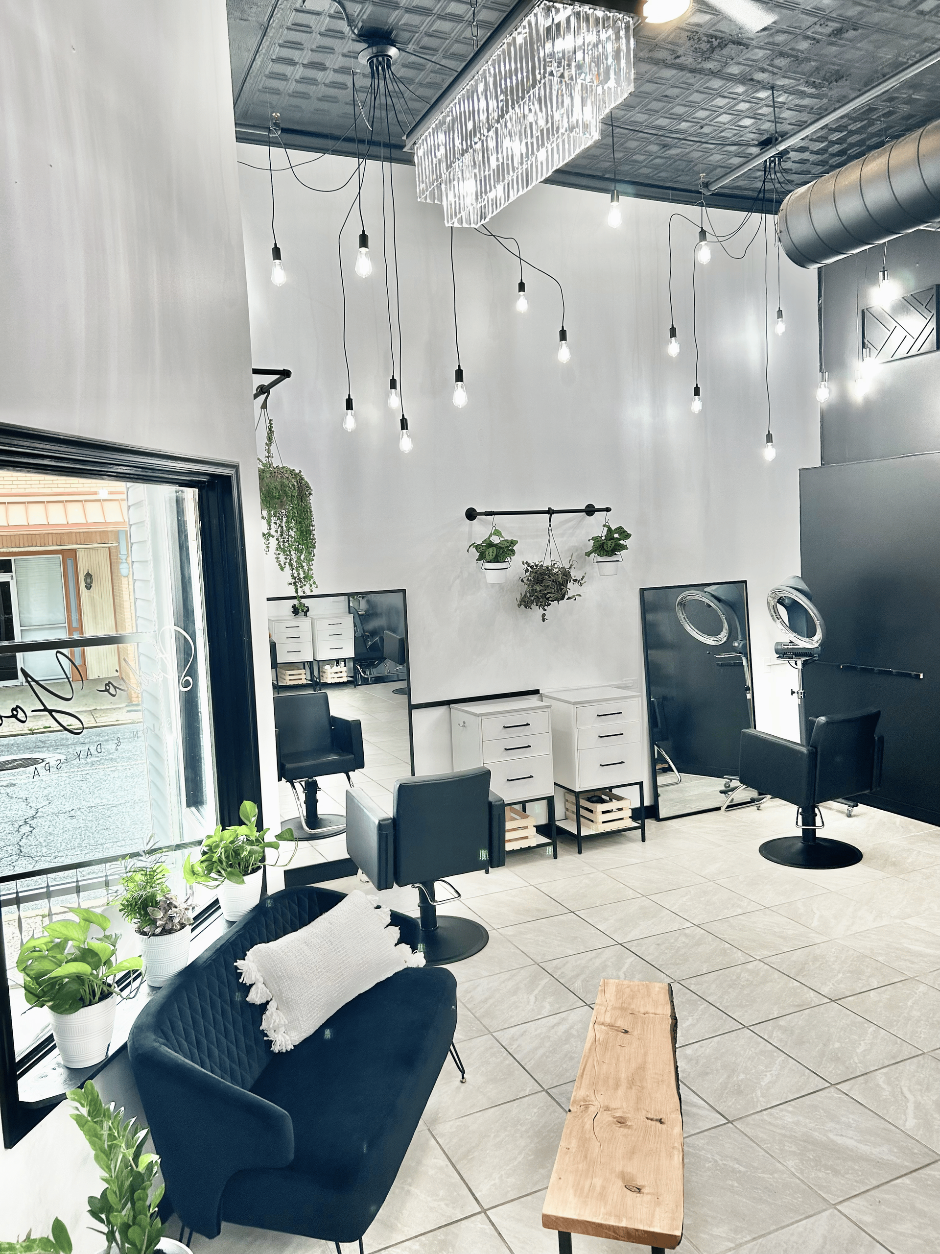 A salon with a couch , chairs , mirrors and plants.