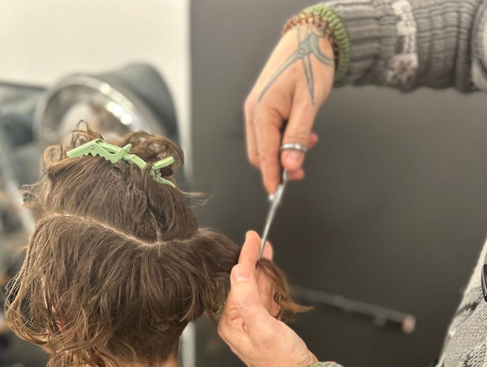 Hands cutting hair with scissors and a comb at a salon, dark hair in focus.