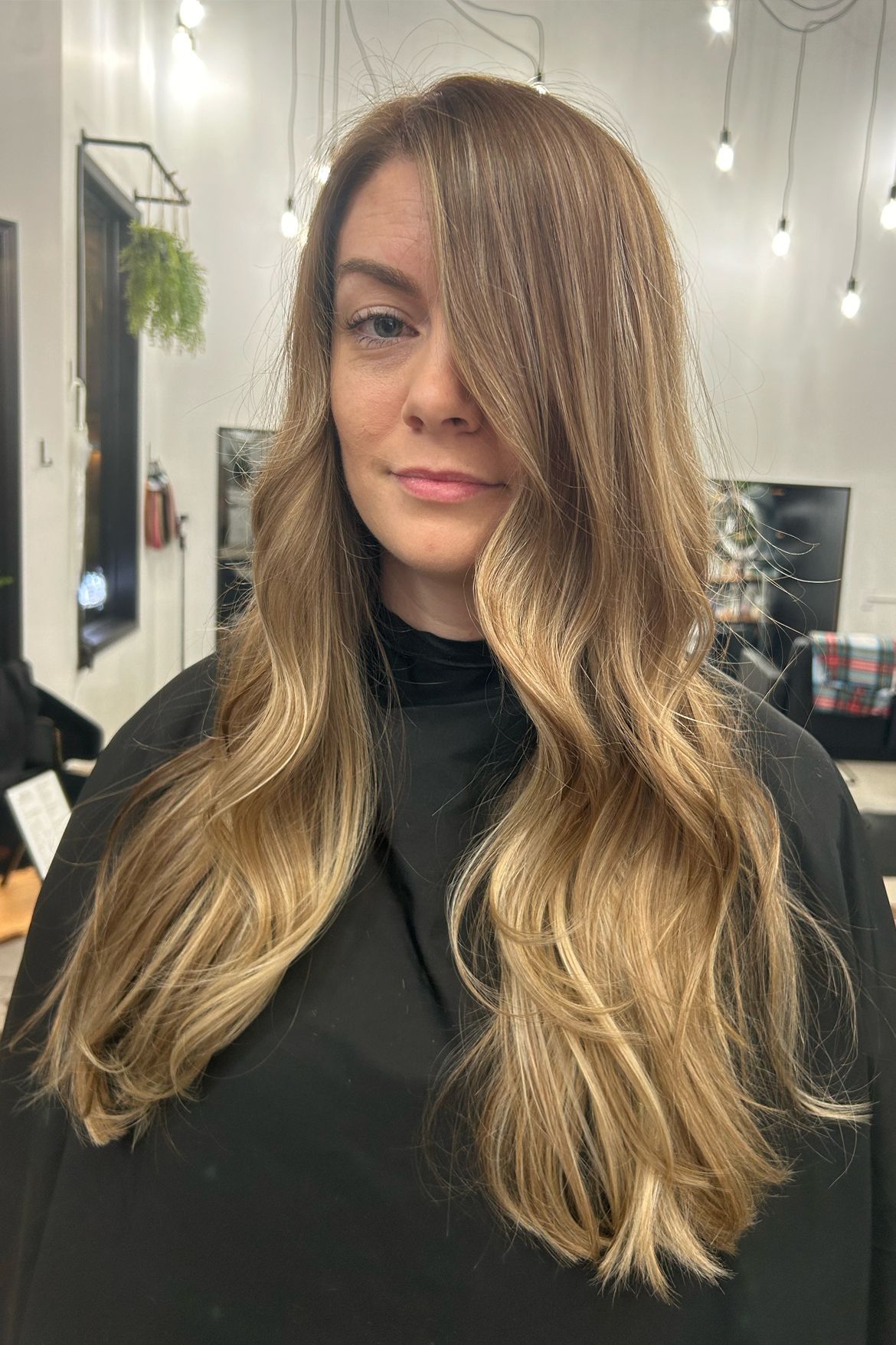 Woman with long wavy hair, golden highlights. Standing inside a salon.